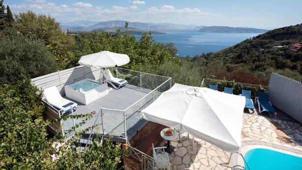 Eine Dachterrasse mit Whirlpool, Liegestühlen und Sonnenschirmen mit Blick auf einen See.
