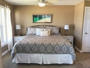 A bedroom with a bed, two bedside tables, a ceiling fan, and a wall-mounted picture. - Surf Side Six C-3 (St Augustine Beach)