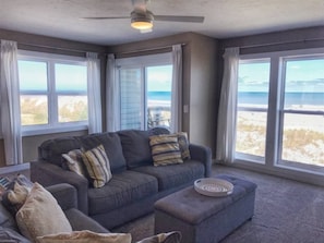 A living room with a grey sofa, ottoman, and a ceiling fan. - Surf Side Six C-3 (St Augustine Beach)