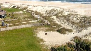 Strandudsigt med et træhegn, et sandområde og en bygning med tag.