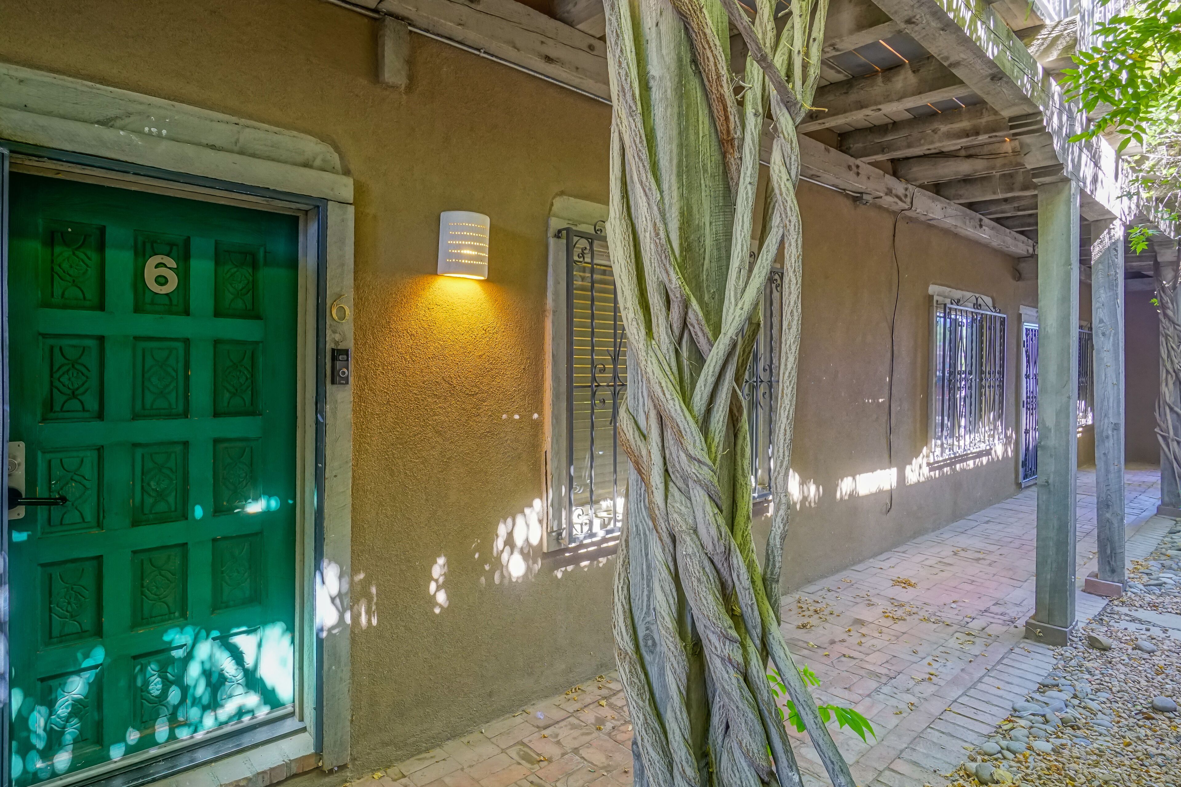 A building with a green door marked with the number 6, a wall-mounted light, and a tree with twisted branches.