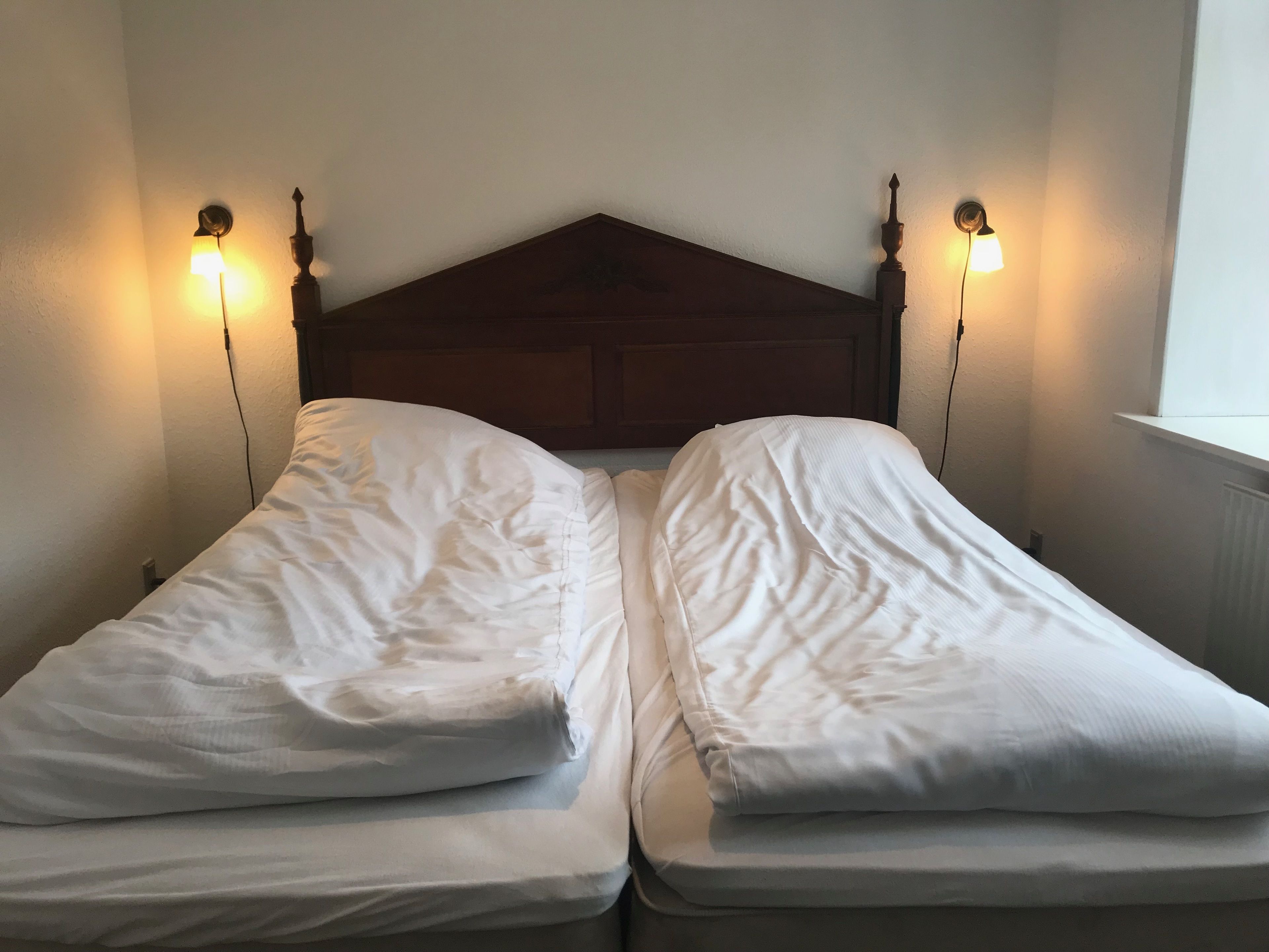 Una cama con dosel de madera, dos lámparas de noche y una ventana a la derecha.