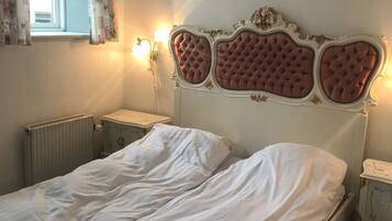 Ein Schlafzimmer mit einem Bett, einem Nachttisch, einer Wandleuchte und einem Fenster mit floralem Vorhang.