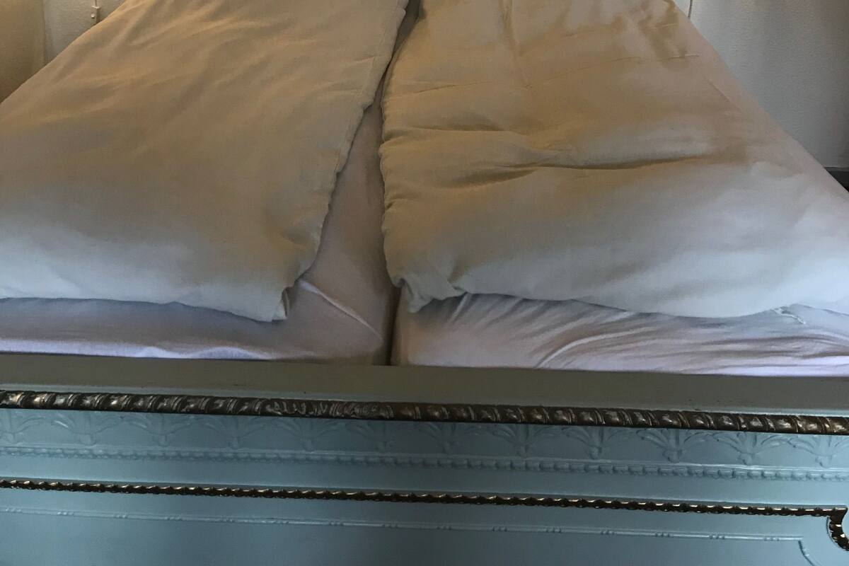 Uma cama com cabeceira, dois apliques de luz na parede e uma parede lisa.