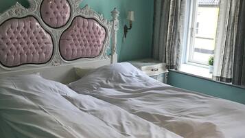 Un letto con testiera imbottita, un comodino con una lampada e una finestra con tende.