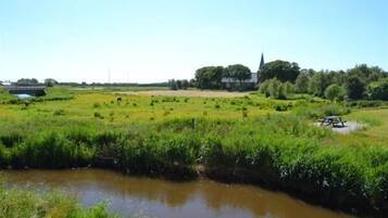 Ett lantligt landskap med en flod, gröna fält, en kyrka och en bro.