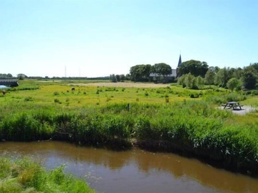 A rural landscape with a river, green fields, a church, and a bridge.