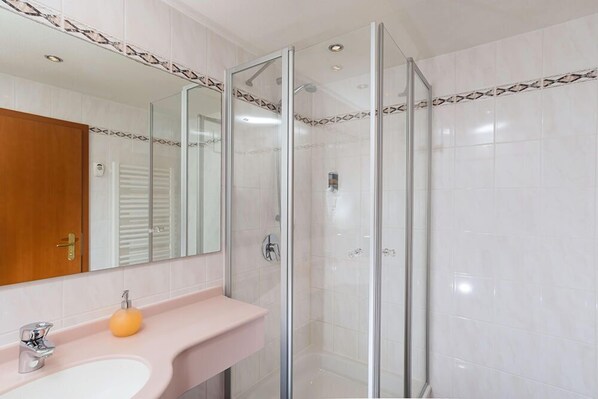 Ein modernes Badezimmer mit einer gläsernen Duschkabine, einem pinkfarbenen Waschbecken und einer Holztür.