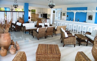 Un amplio salón con muebles de mimbre, una barra con taburetes blancos y jarrones decorativos.