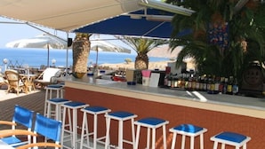 Un bar situé en bord de mer, avec une terrasse, un comptoir et une vue sur l’océan.