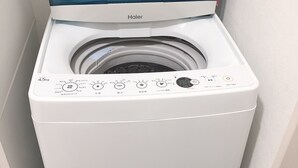 En vit tvättmaskin från Haier med frontmatning, genomskinlig topp, kontrollpanel och en ansluten slang.