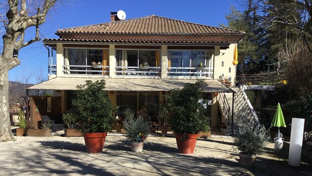 Une maison à deux étages dotée d’un balcon, entourée de plantes en pot.