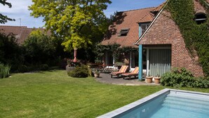 Ett hus byggt av tegel med en swimmingpool, en täckt uteplats och en gräsmatta.