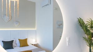 Moderni hotellihuone, jossa on sänky, yöpöytä, lamppu, seinätaide ja ruukussa oleva kasvi.