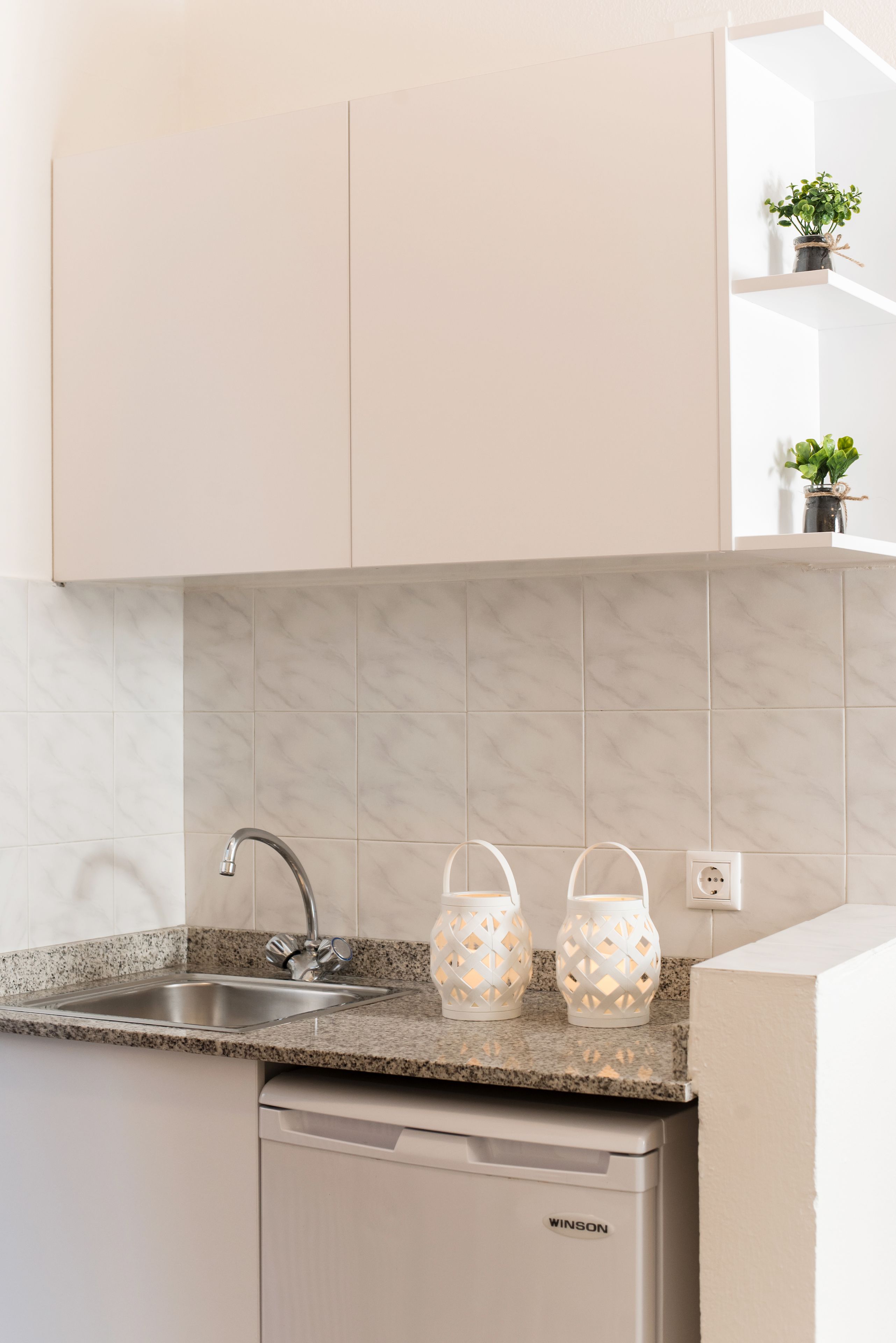 Cocina con encimera de granito, pileta integrada y lavavajillas. Hay dos faroles decorativos en la encimera.