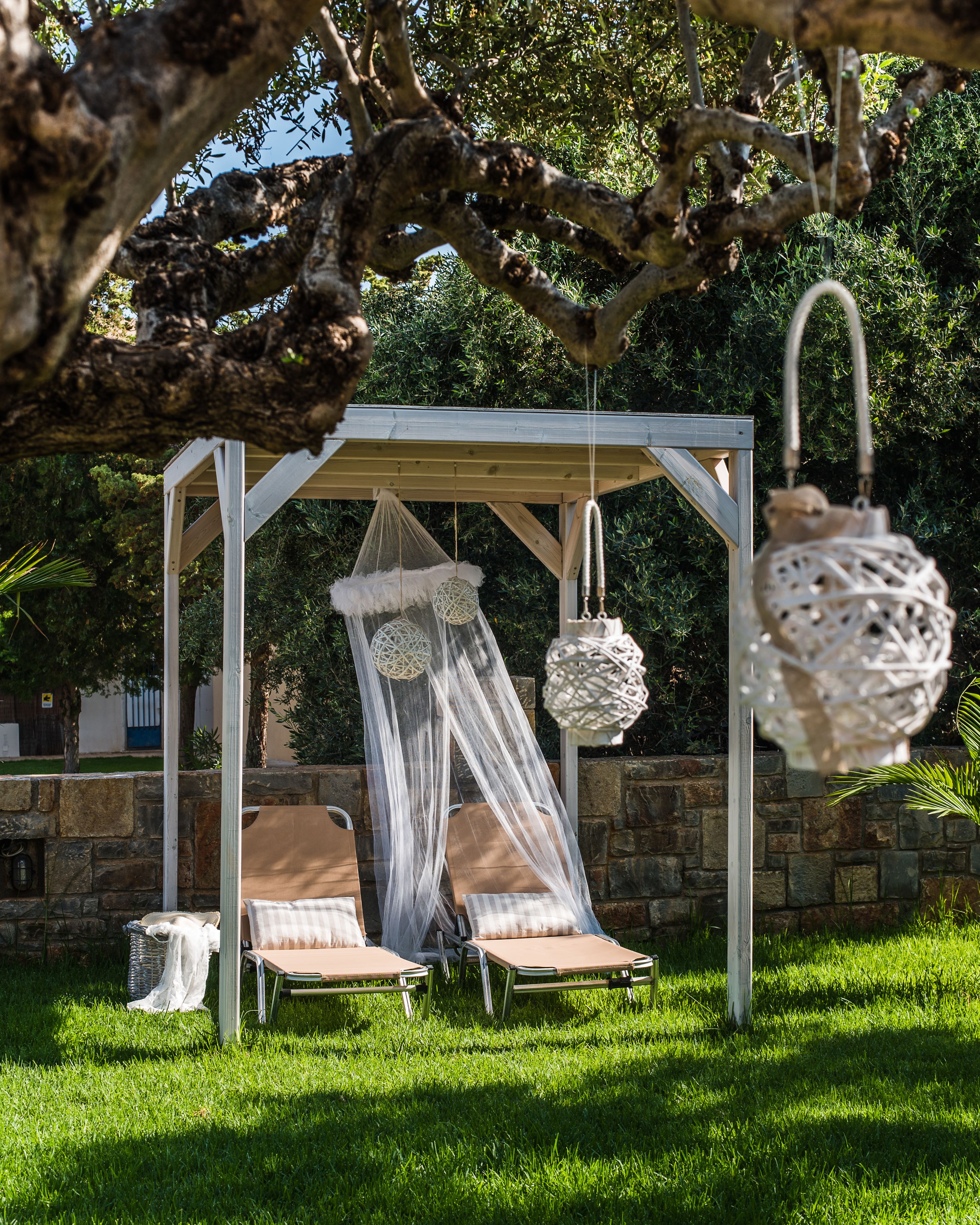 A gazebo with a canopy, two lounge chairs, and hanging lanterns.