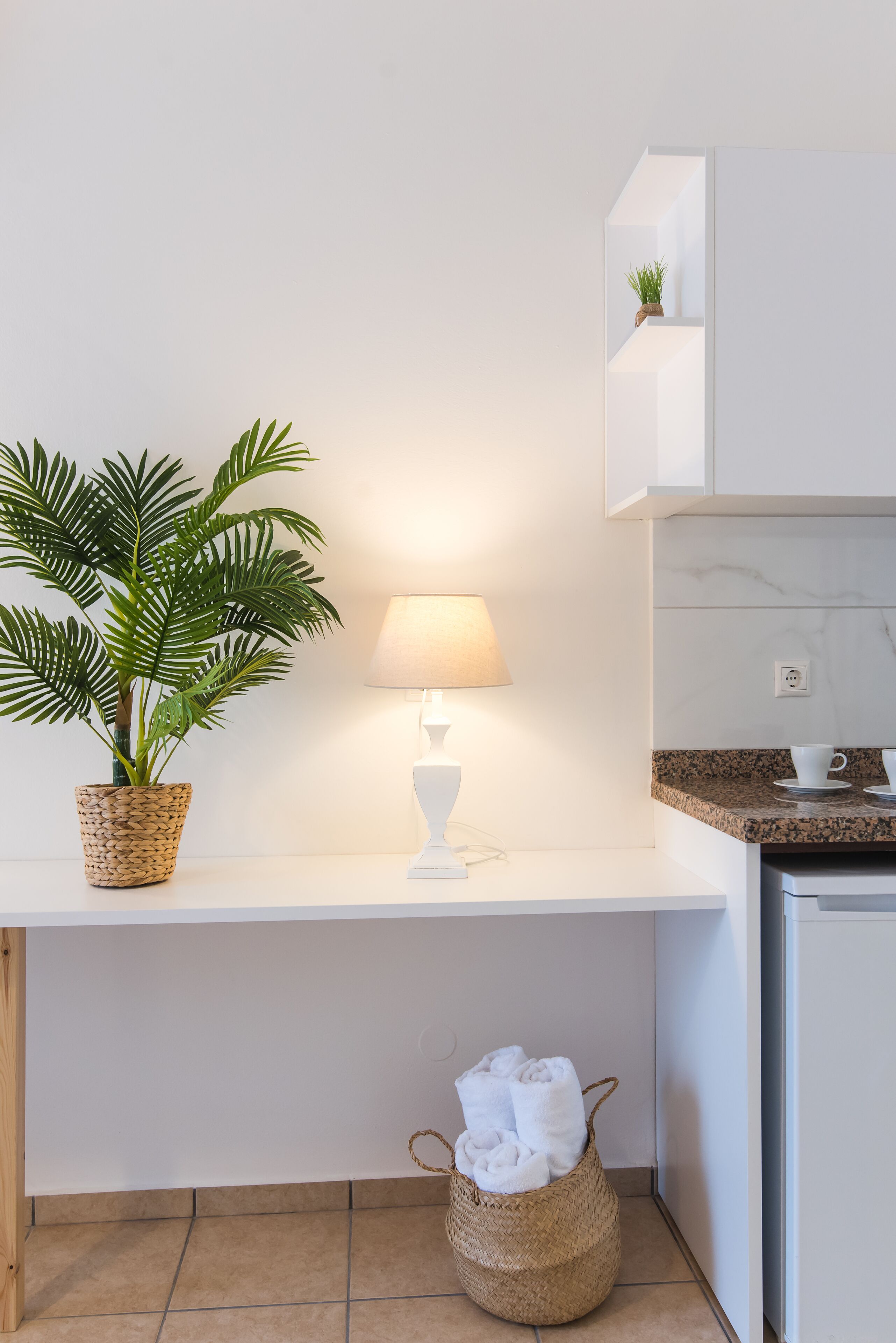 Une cuisine moderne avec un plan de travail blanc, une plante en pot, une lampe et un panier contenant des serviettes.