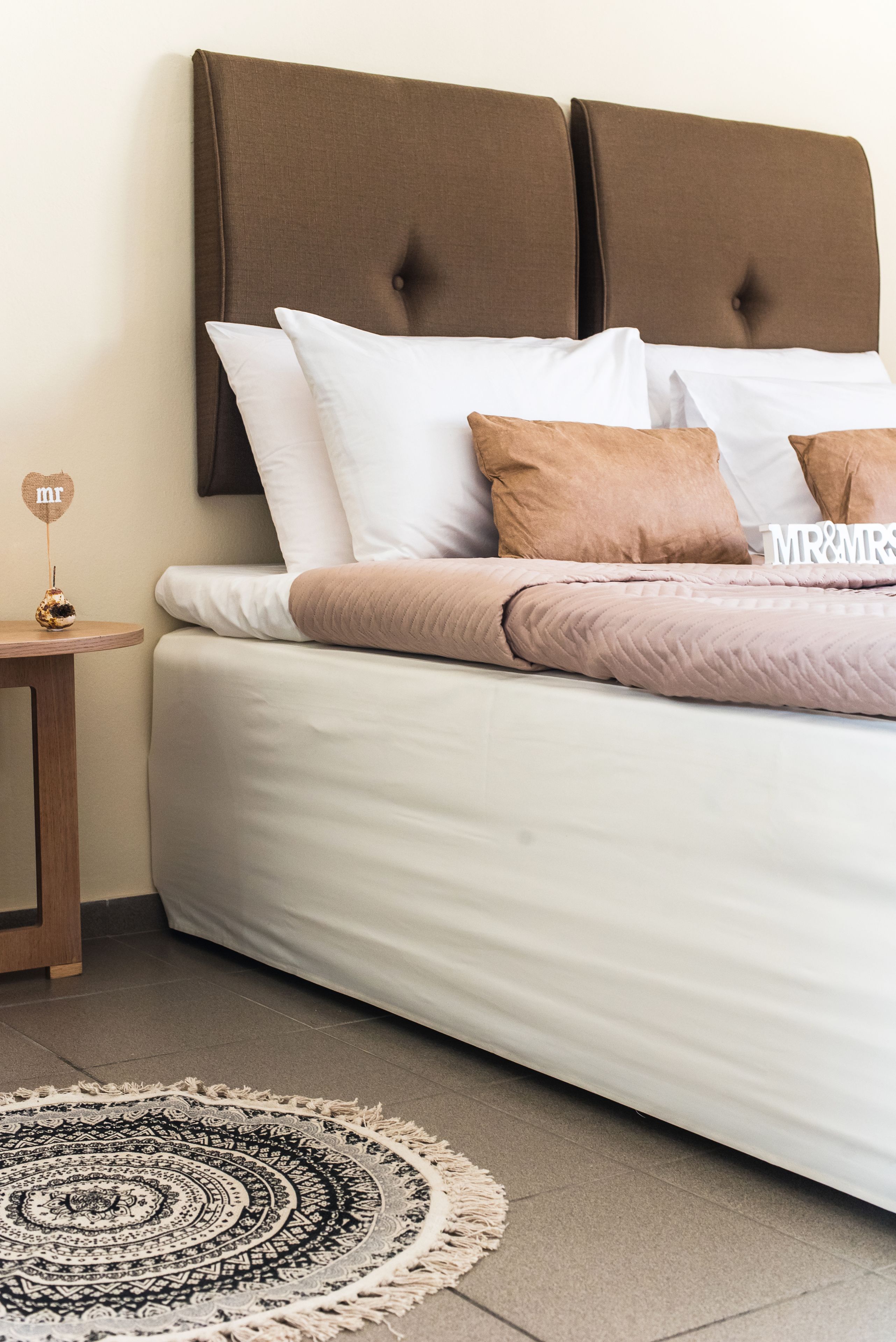 A neatly made bed with a brown headboard, white and brown pillows, and a decorative sign.