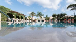 A clear swimming pool with lounge chairs and umbrellas, surrounded by palm trees and a clear sky. - Mirage Studios (Hersonissos)