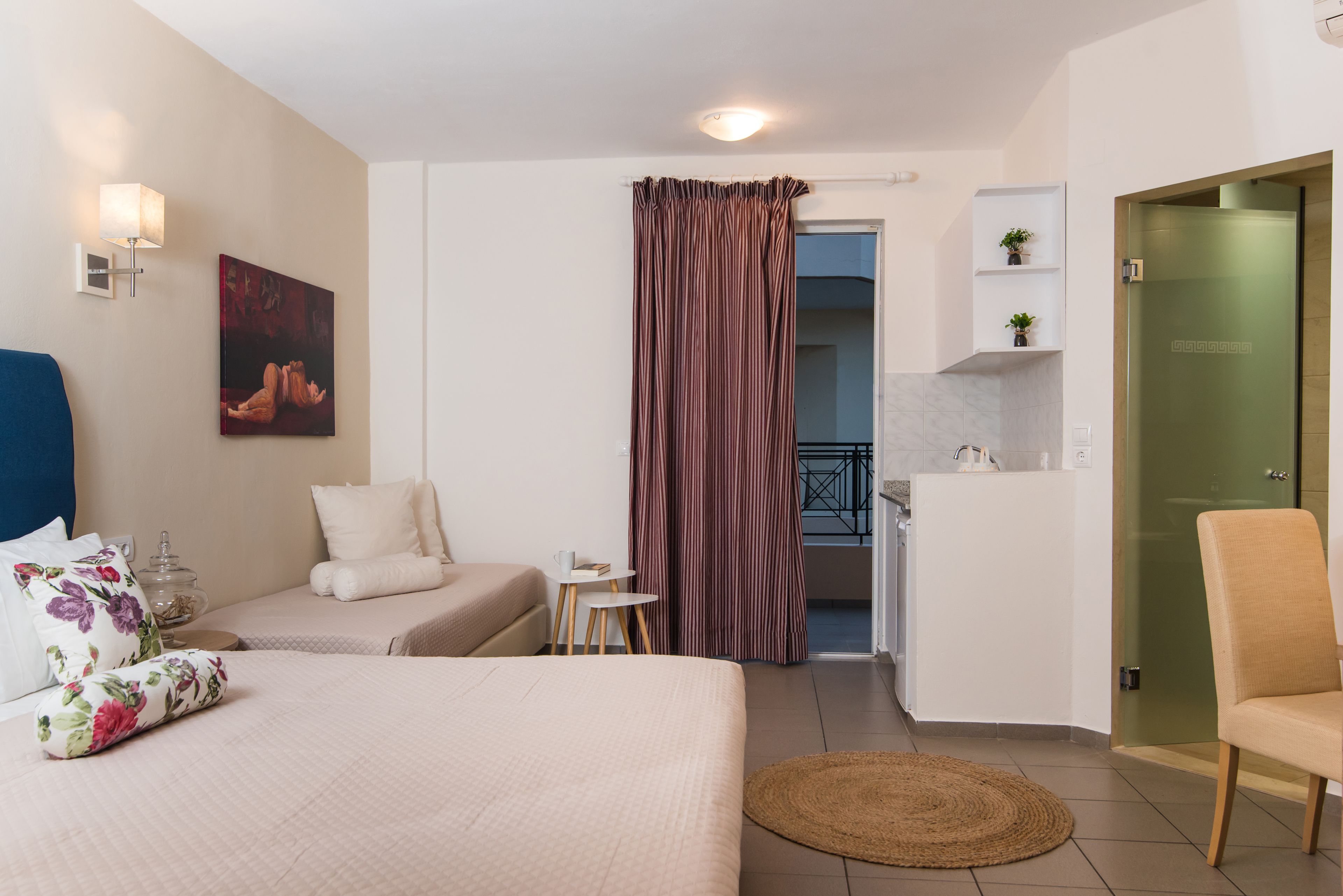 A hotel room with a bed, two bedside tables, a small desk, a chair, a painting, a curtain, and a view of the balcony.