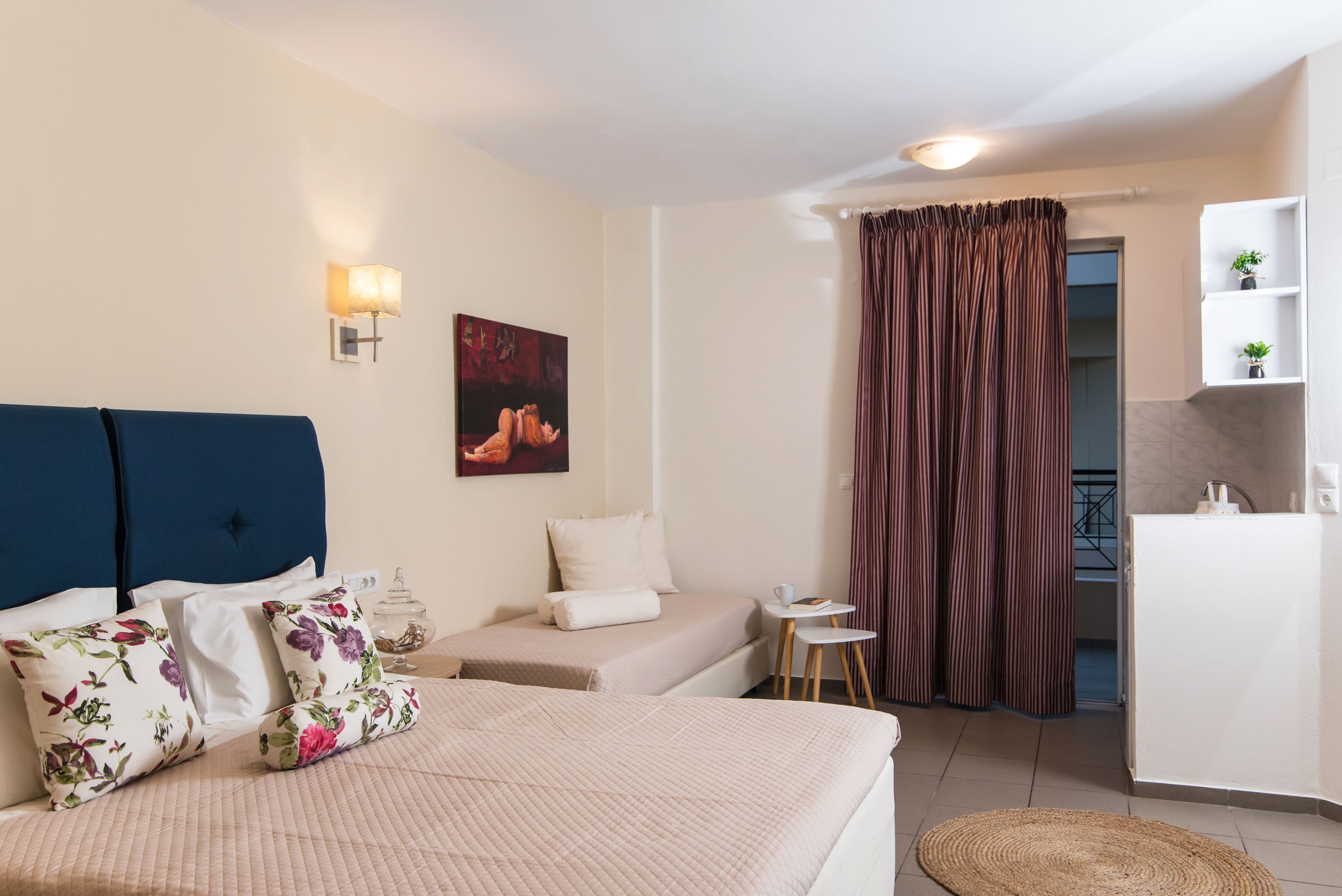 A hotel room with a bed, a small desk, a chair, a nightstand, a lamp, a painting, and a bathroom visible through a curtain.