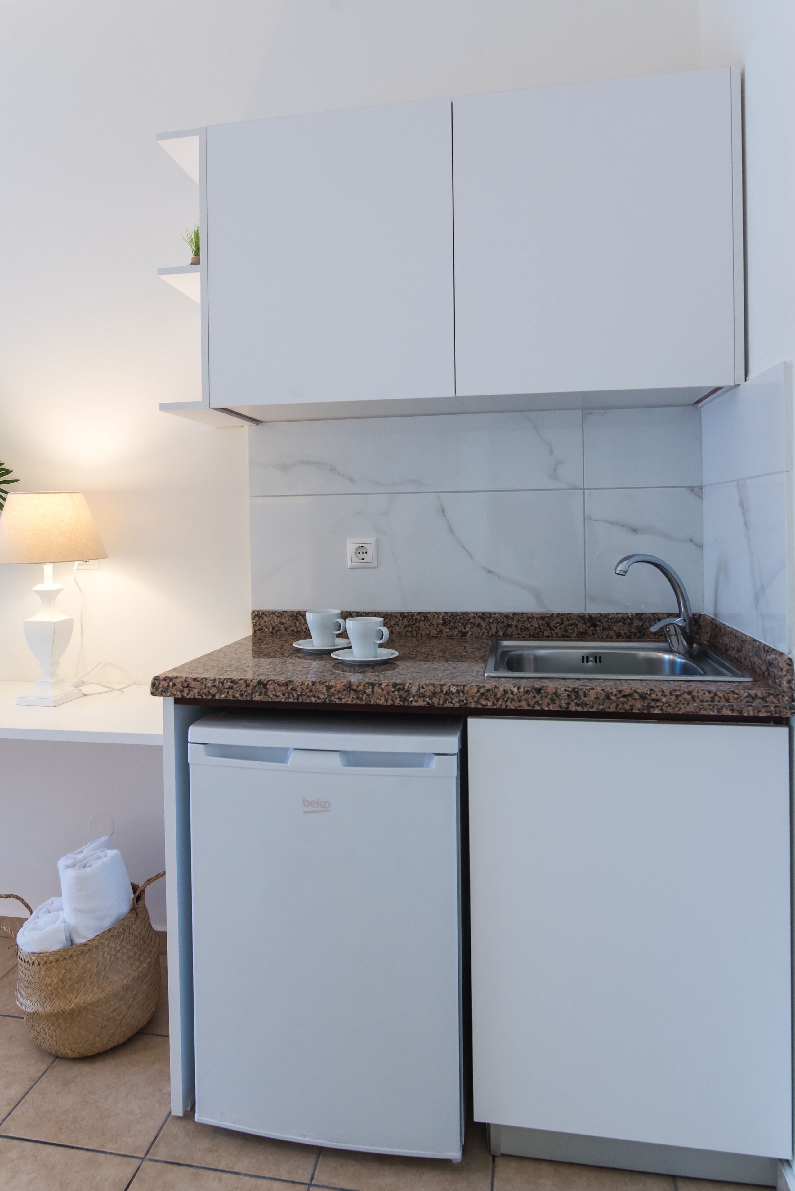Une cuisine compacte avec des meubles blancs, un plan de travail en granit, un évier encastré et un petit lave-vaisselle.
