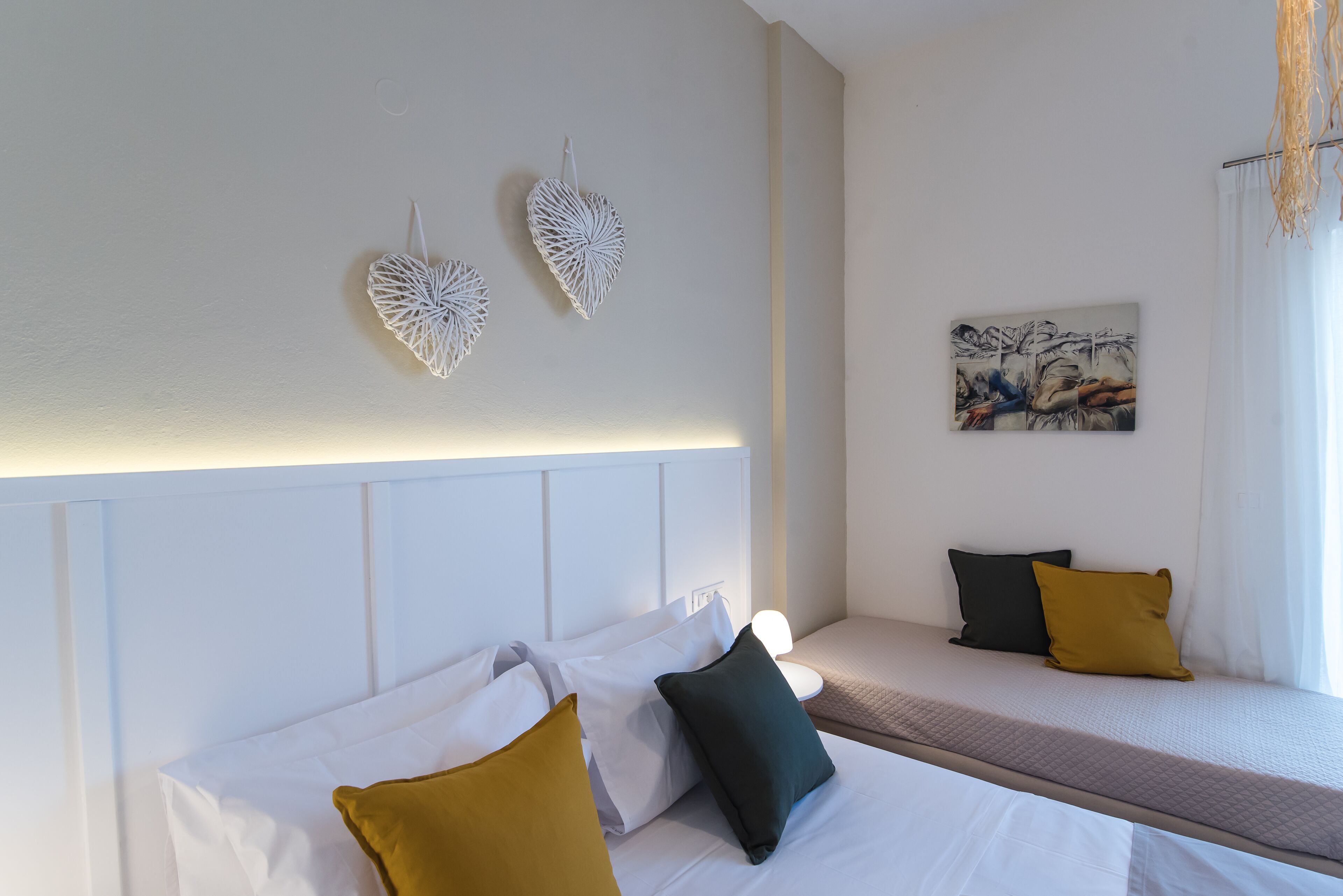 Una habitación de hotel con cama, mesita de noche, un cuadro colgado en la pared y una ventana con cortinas.