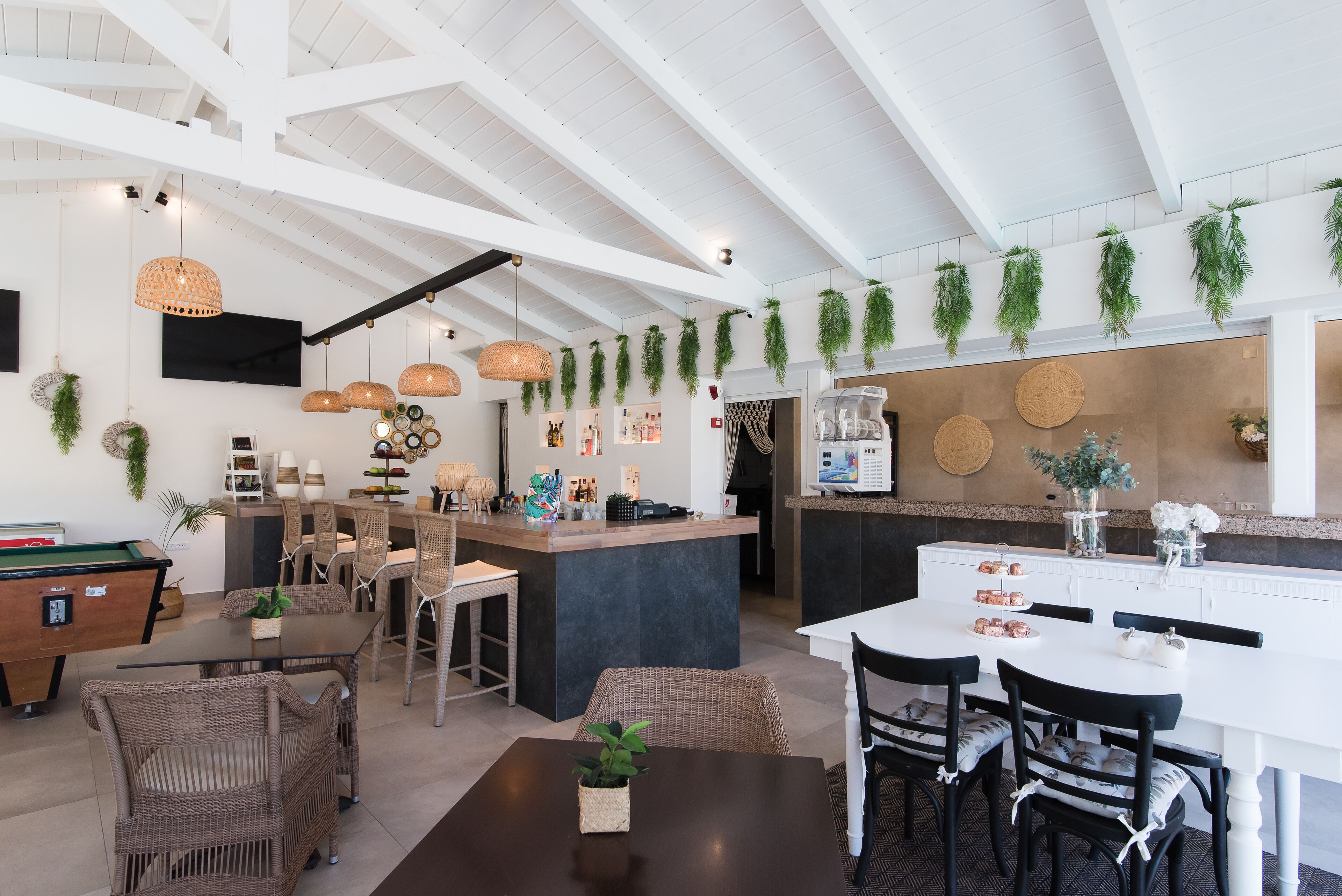 Una cocina moderna con una isla central, comedor con sillas de mimbre y plantas colgantes.