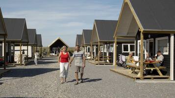 A row of beach huts with a gravel ground, wooden benches, and a clear sky.