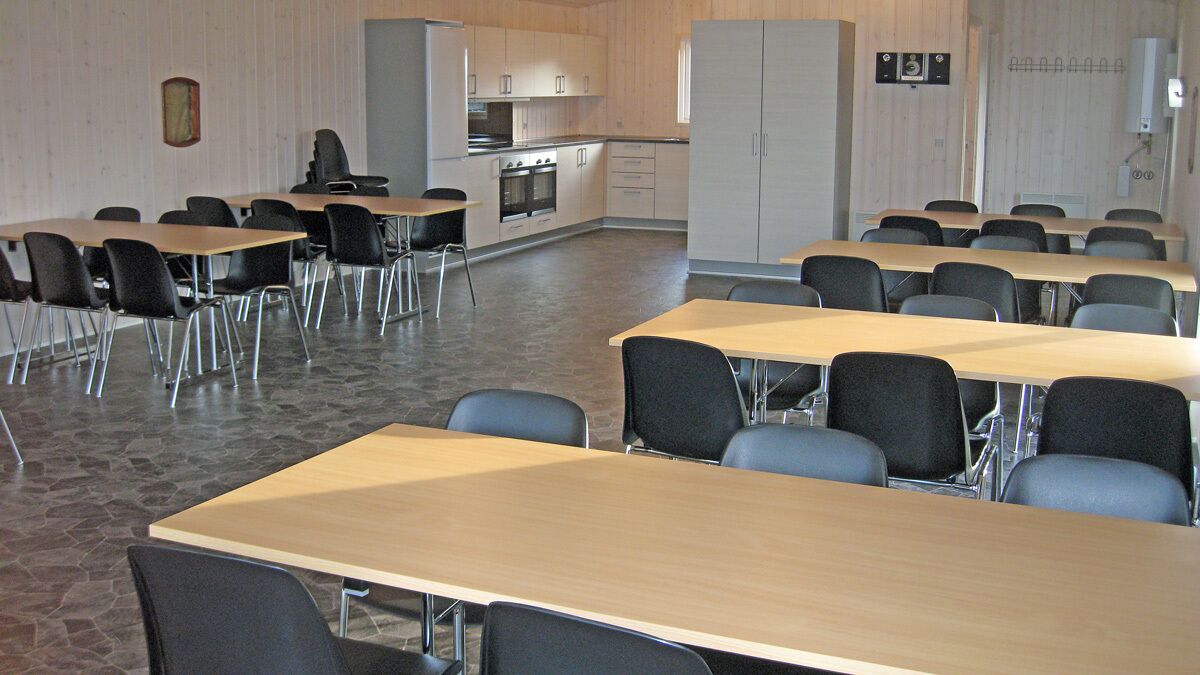Une salle de conférence équipée de plusieurs tables et chaises, d’un coin cuisine et d’une grande armoire.