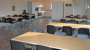 A conference room with multiple tables and chairs, a kitchenette, and a large cabinet.