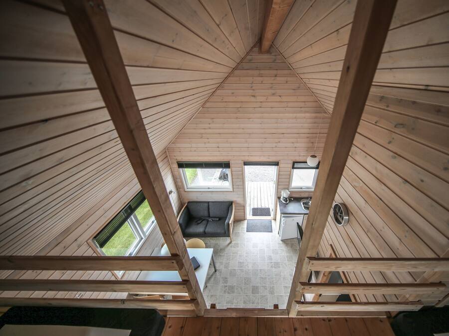 A wooden interior with a sloped ceiling, a sofa, a small table, and a kitchenette area.