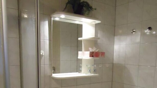 A bathroom with a white sink, a mirror, and a shelf with toiletries. - Pension Thaler Hof (Thale)