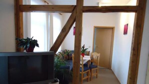 A cozy living room with a television, wooden beams, a dining area with a table and chairs, and potted plants. - Pension Thaler Hof (Thale)