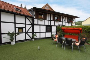 Una casa tradicional con entramado de madera y techo rojo, un patio con césped artificial y mobiliario de exterior.