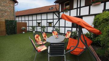 Eine einladende Terrasss mit einem runden Tisch und Stühlen, umgeben von einem gepflegten Rasen und einem Gebäude mit freiliegenden Holzbalken und einem Ziegeldach.