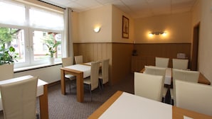 A hotel dining area with tables and chairs, a window with a view of the street, and a wall-mounted light fixture. - Pension Thaler Hof (Thale)