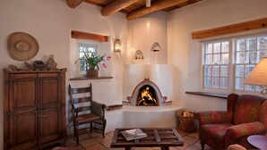 A cozy living room with a fireplace, wooden furniture, and a window with a view. - One Bedroom, Two Bath, Sunset Views & Kiva Fireplaces. Walk Downtown! (Santa Fe)
