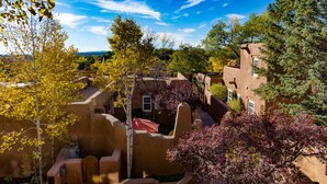 A courtyard with stucco buildings, trees, and a clear sky. - One Bedroom, Two Bath, Sunset Views & Kiva Fireplaces. Walk Downtown! (Santa Fe)