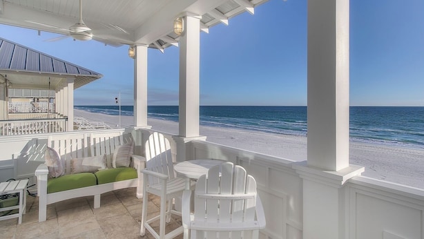 A covered outdoor seating area with white chairs and a table, overlooking a beach. - Direct Gulf Front + Private Walk Down Sleeps 12  (Panama City Beach)