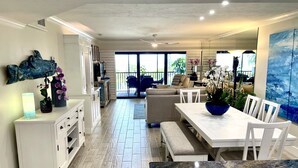 Una cocina moderna con armarios blancos, un comedor con encimera de mármol y vistas al exterior a través de amplios ventanales.