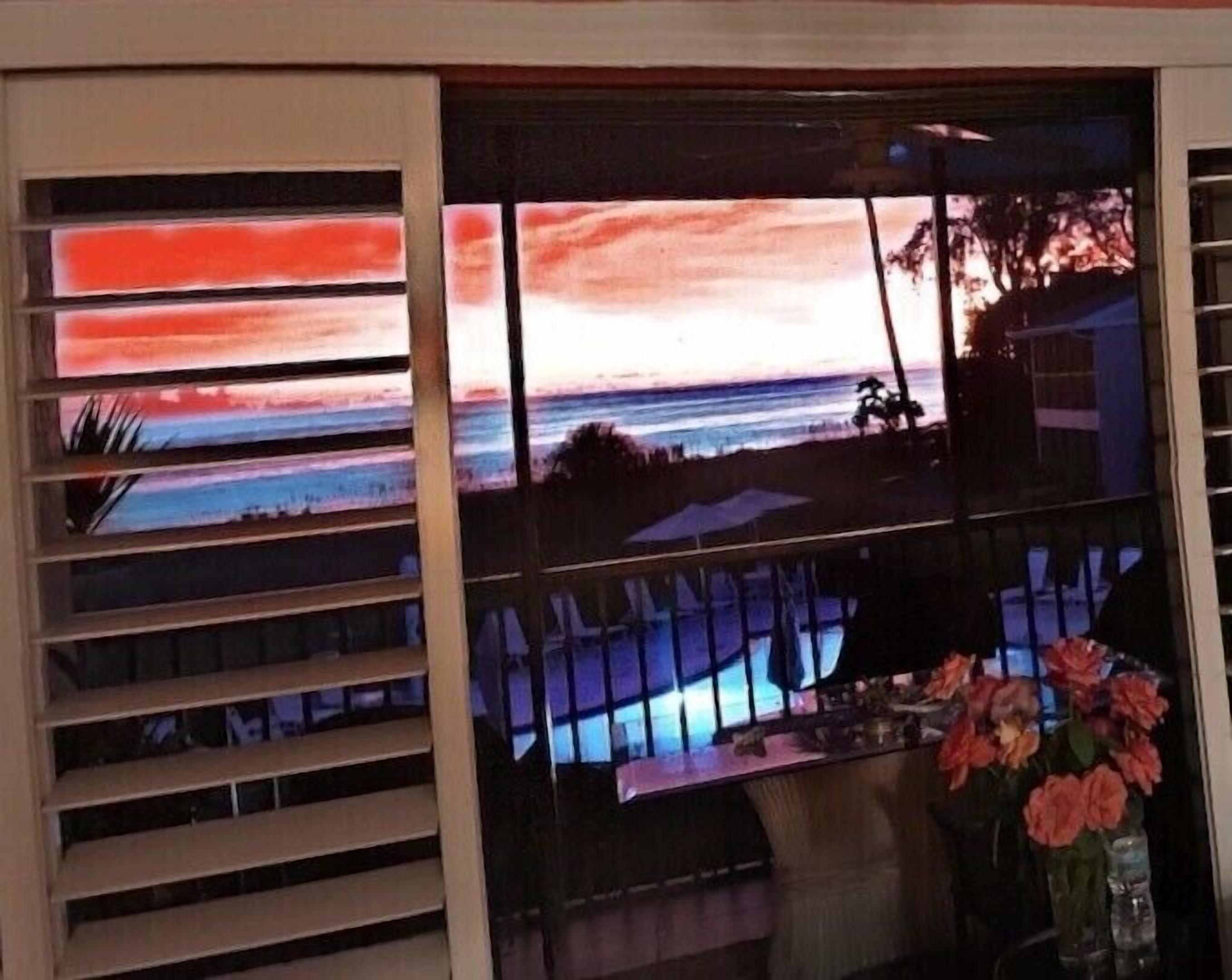 Ein Zimmer mit Meerblick bei Sonnenuntergang, einem Esstisch und einer Vase mit Blumen.