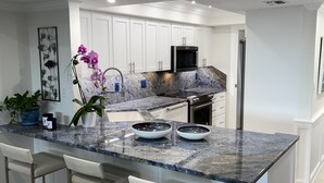 Una cocina moderna con armarios blancos, encimeras de granito y electrodomésticos de acero inoxidable.