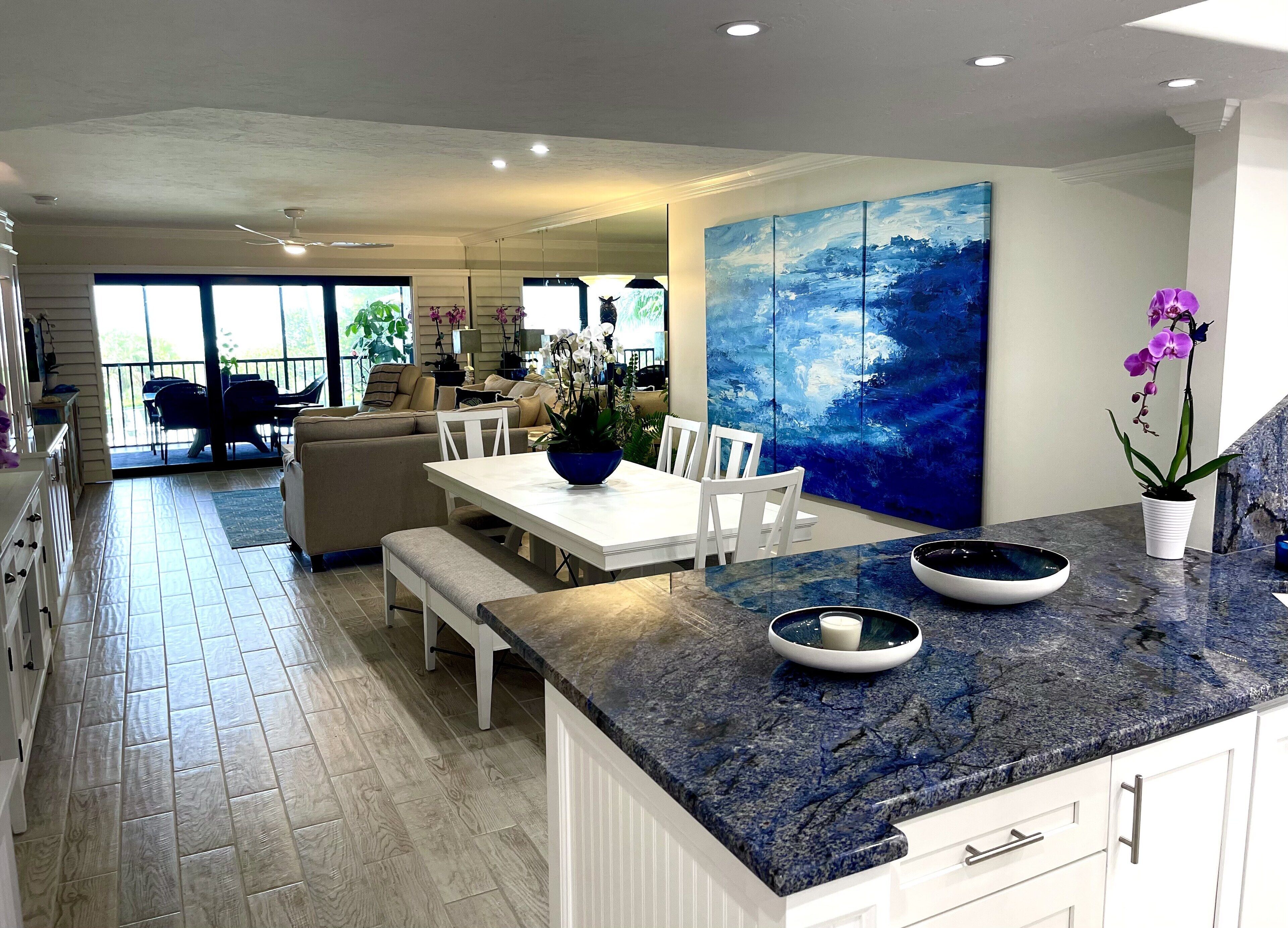 A modern kitchen with a marble countertop, white cabinetry, and a large blue painting on the wall.