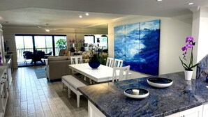 Una cocina moderna con encimera de mármol, armarios blancos y un cuadro azul grande en la pared.
