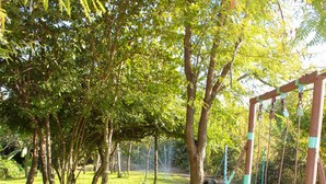 Un parque infantil con columpios y un tobogán, rodeado de árboles y césped.
