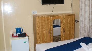 Un dormitorio con cama, un armario de madera, un refrigerador blanco pequeño, un televisor montado en la pared y una mosquitera sobre la cama.