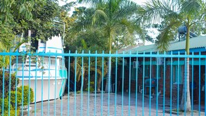 Un área cercada con un bote, palmeras y un edificio de techo azul.