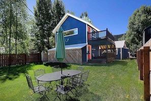 A blue house with a deck, a fenced backyard, and a table with chairs.