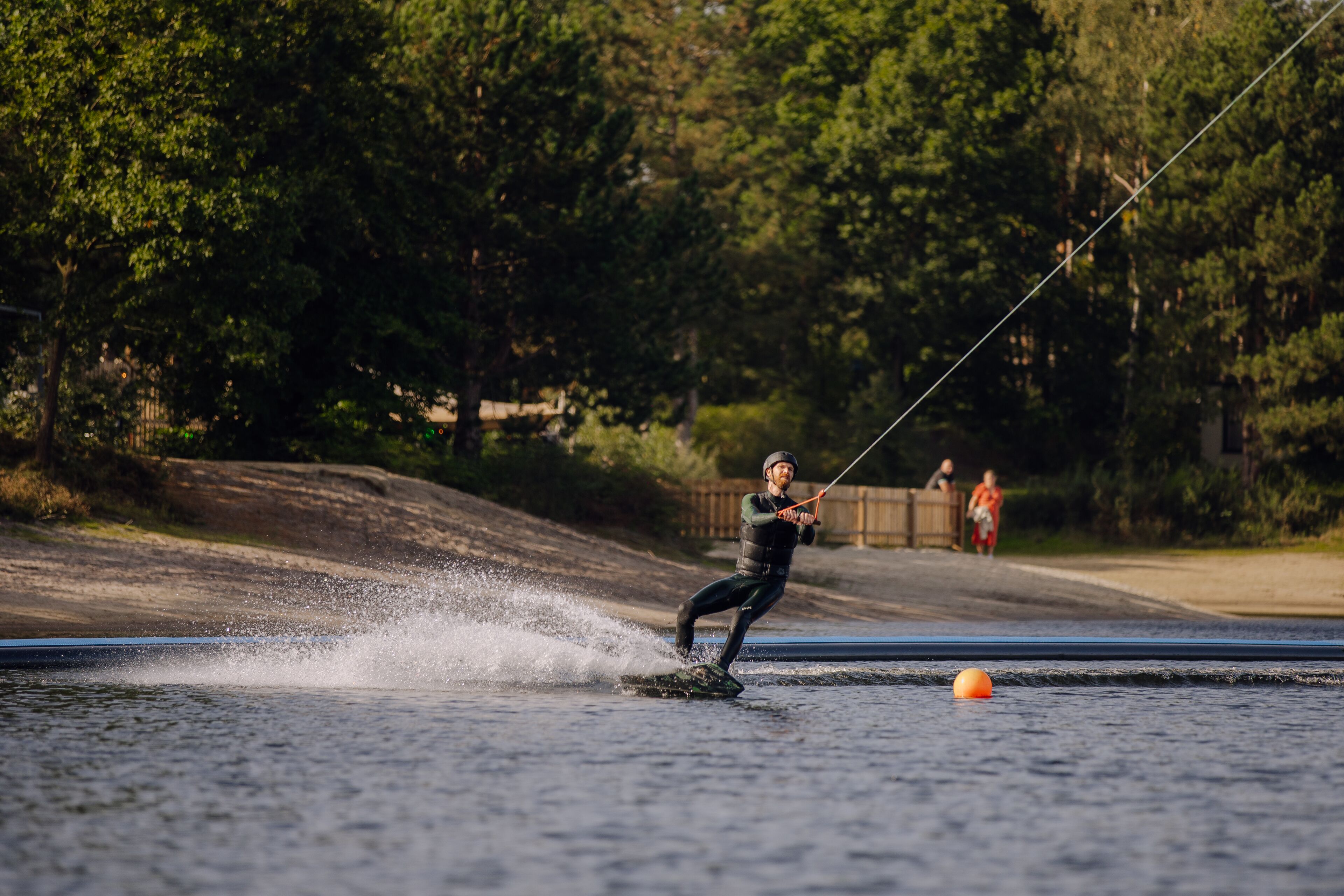 Uma pessoa praticando wakeboard em um corpo d'água, com árvores ao fundo.